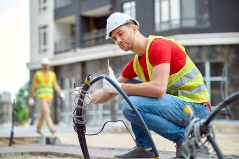 Konzentrierter und erfahrener Bauarbeiter mit Baumwollhandschuhen installiert elektrische Leitungen.
