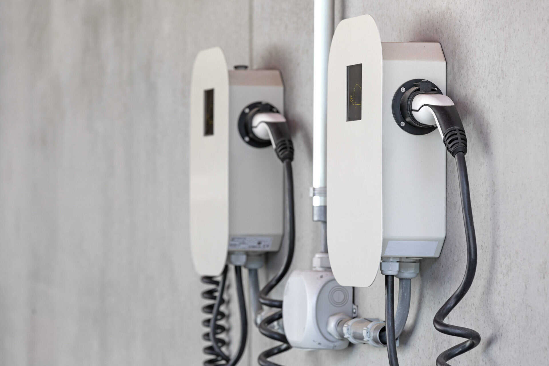 Zwei moderne Wallboxen für Elektrofahrzeuge sind an einer Betonwand montiert, mit angeschlossenen Ladekabeln. Symbol für nachhaltige Elektromobilität und effiziente Ladeinfrastruktur.