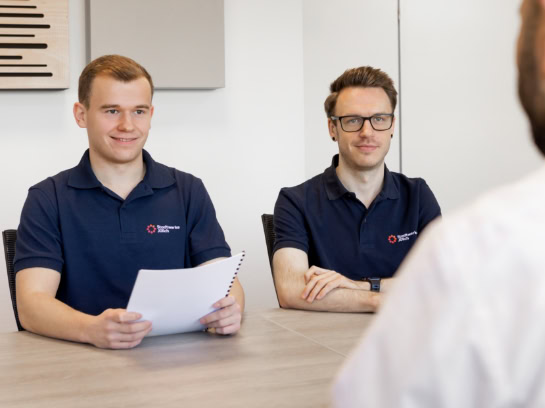 Zwei junge Mitarbeiter der Stadtwerke Jülich sitzen an einem Tisch in einem modernen Büro. Einer der Mitarbeiter hält ein Dokument in seinen Dokumenten.
