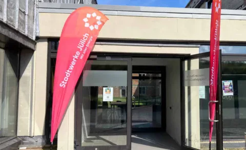 Rote Beachflag mit Stadtwerke-Jülich-Logo vor einem geöffneten Eingangsbereich.