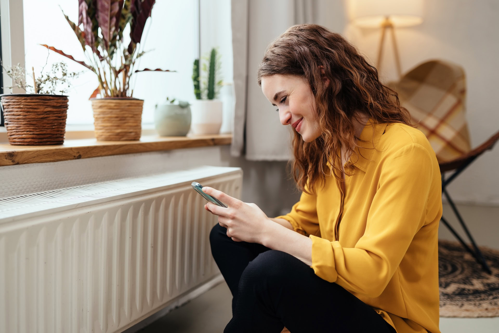 Junge Frau bedient mit ihrem Smartphone eine Heizung – Symbol für moderne, komfortable Gasversorgung.