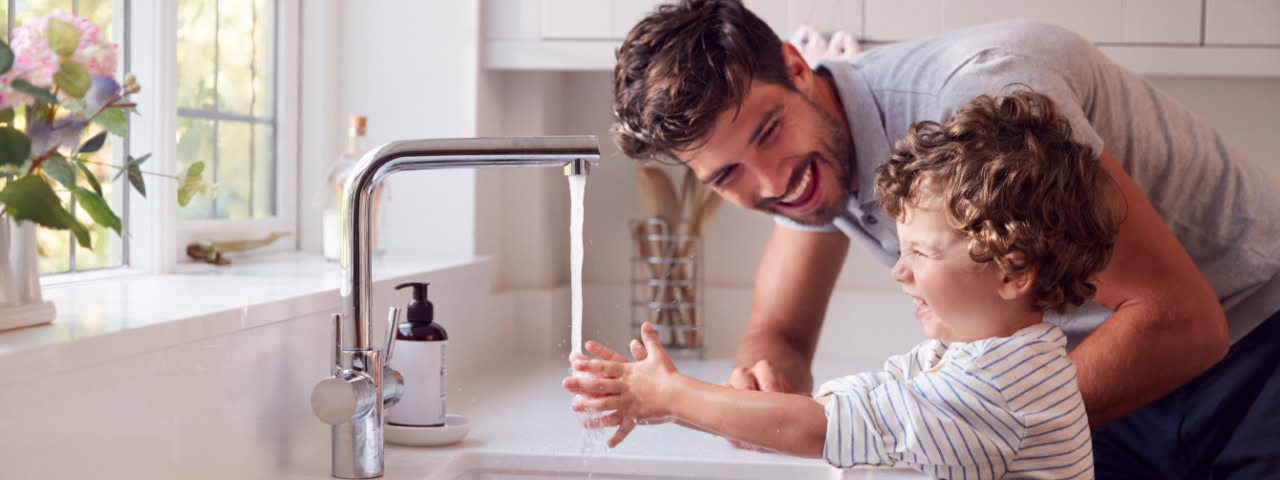 Vater hilft seinem Kind beim Händewaschen am Wasserhahn – Symbol für sicheres, sauberes Trinkwasser im Alltag.