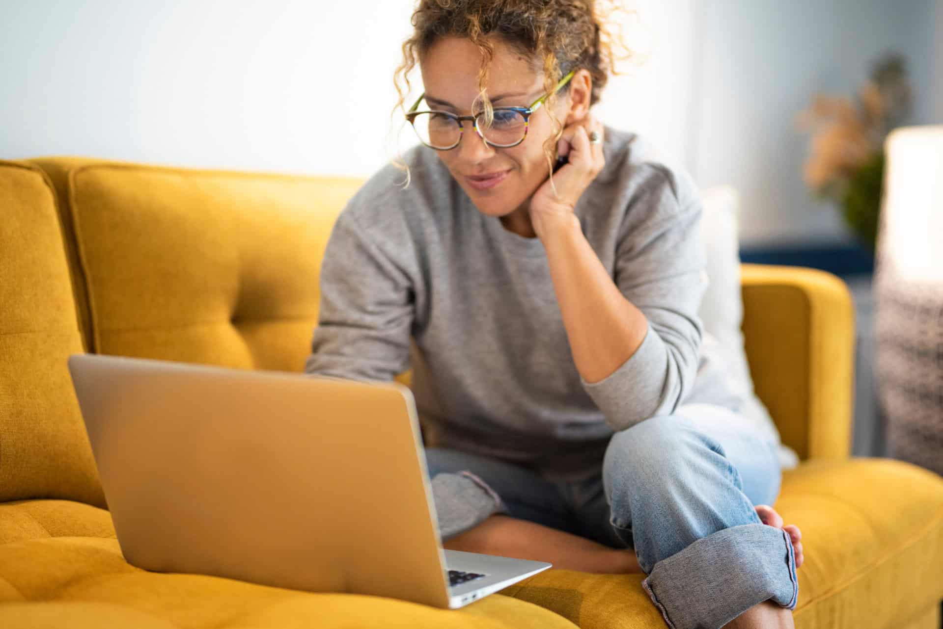 Frau sitzt auf einem gelben Sofa und nutzt ein Laptop – symbolisch für digitale Information und einfachen Zugang zu Neuigkeiten