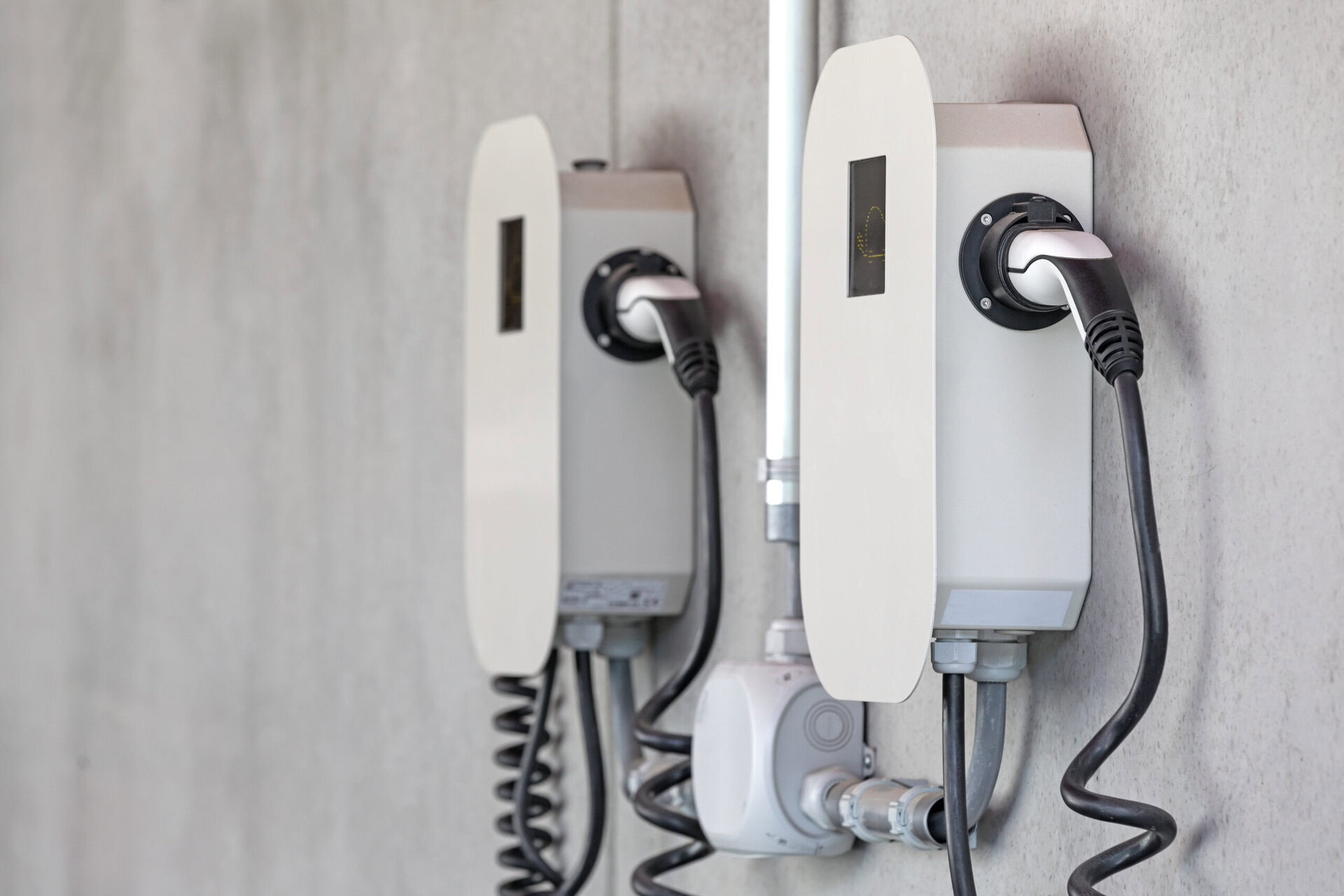 Zwei moderne Wallboxen für Elektrofahrzeuge sind an einer Betonwand montiert, mit angeschlossenen Ladekabeln. Symbol für nachhaltige Elektromobilität und effiziente Ladeinfrastruktur.