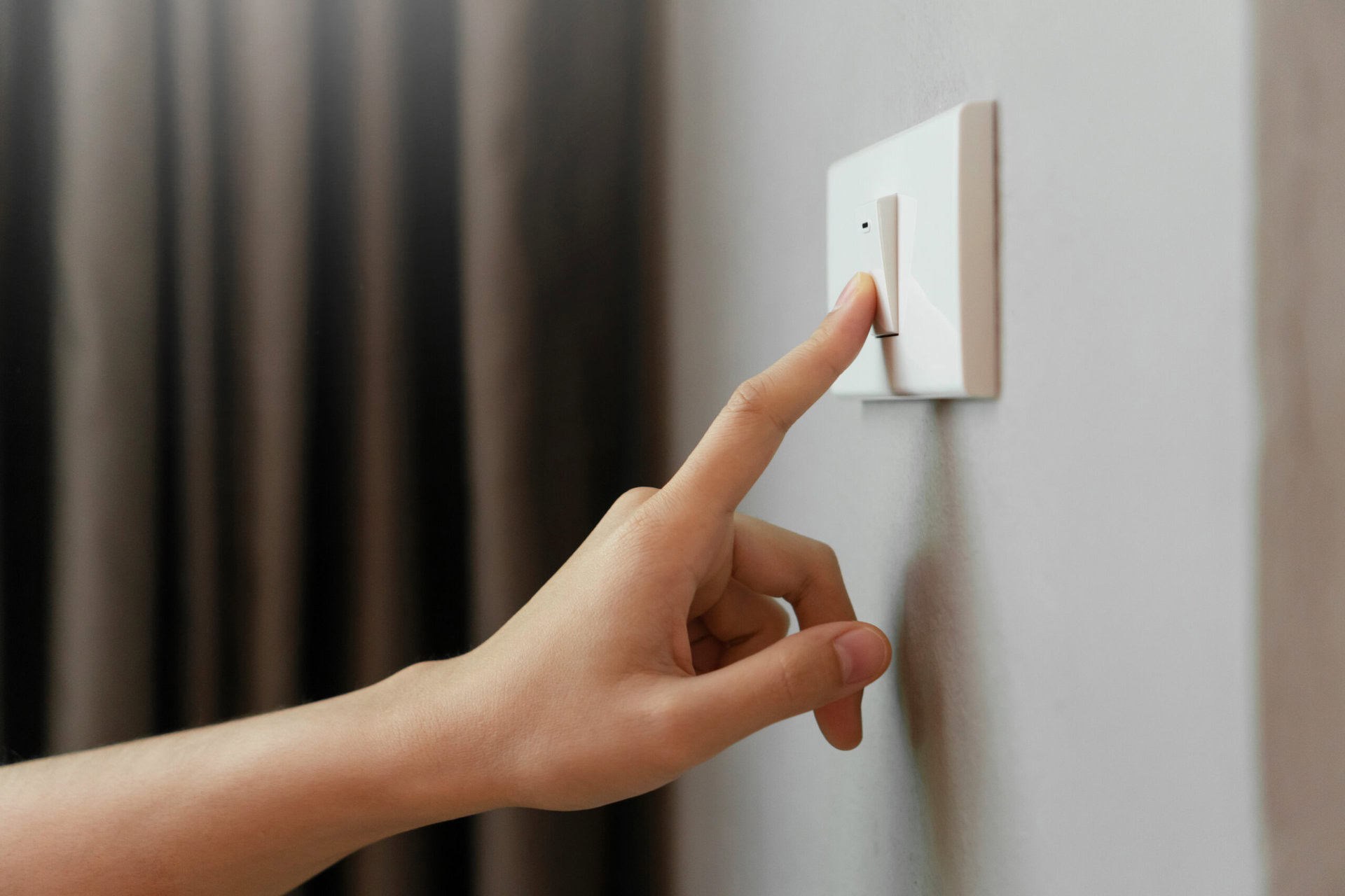 Nahaufnahme eines weiblichen Fingers, der einen Lichtschalter zu Hause ausschaltet. Symbol für Energieeinsparung und bewussten Stromverbrauch.