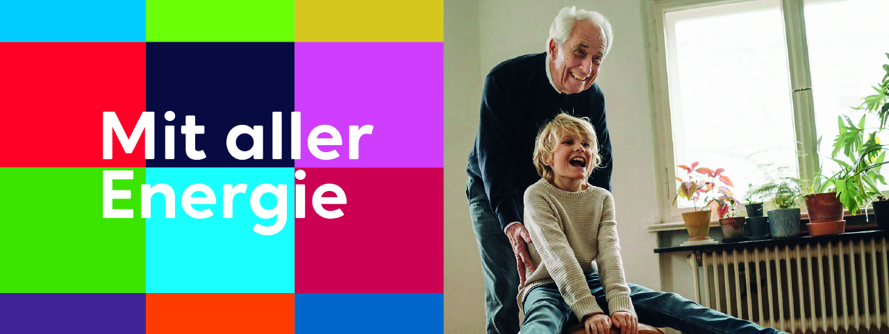 Ein lachendes Kind sitzt auf einem rollbaren Hocker, während ein älterer Mann es mit Freude anschiebt. Links im Bild ist ein farbenfrohes Raster mit dem Schriftzug „Mit aller Energie“. Im Hintergrund stehen Pflanzen auf einer Fensterbank, die eine gemütliche Wohnatmosphäre schaffen.