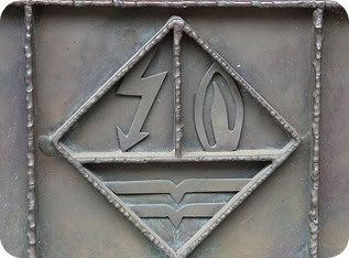 Auf dem Bild ist ein Türgriff zu sehen, auf welchem das alte Logo der Stadtwerke dargestellt wird. Das alte Logo zeigt die Symbole von Gas-, Strom- und Wasserversorgung.