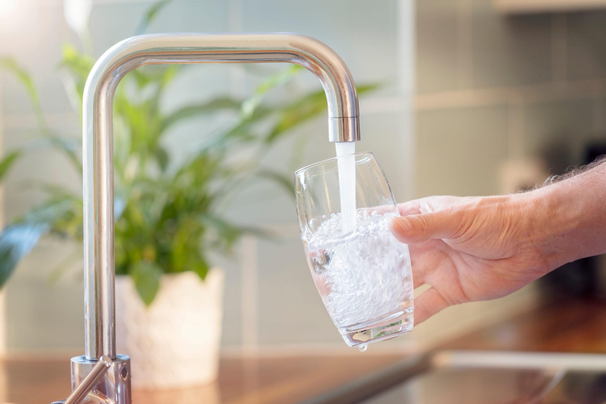 Bild eines Wasserhahns, eine Person hält ein Glas darunter und füllt es mit Trinkwasser.